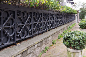Old ornate vintage Metal fence with a green hedge in the city street.